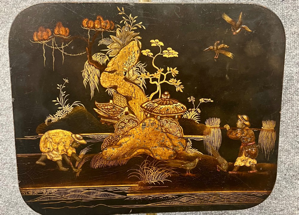 An antique Regency pole screen featuring a black lacquered rectangular panel decorated with gold Chinoiserie landscapes, supported by an adjustable brass rod on an ebonised tri-form base. View II