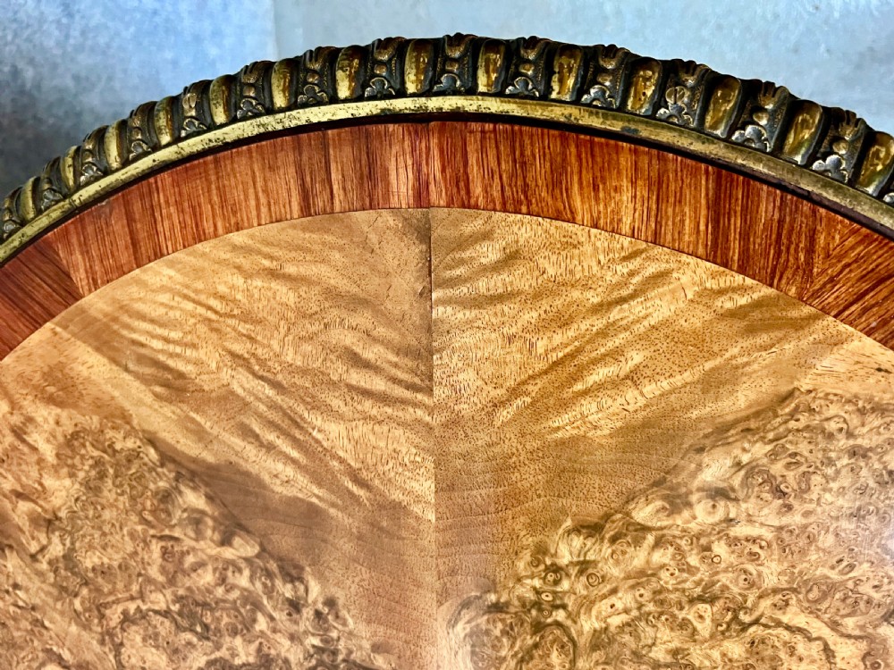 A Victorian burr walnut oval centre table featuring a crossbanded top with brass egg-and-dart moulding above a carved central column and four scrolled legs. View IV