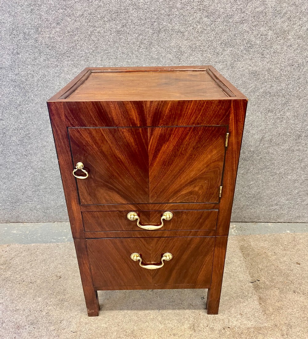 A George III mahogany bedside cabinet featuring a tray top, cupboard door, two drawers with brass swan-neck handles, and brass side carrying handles. View III