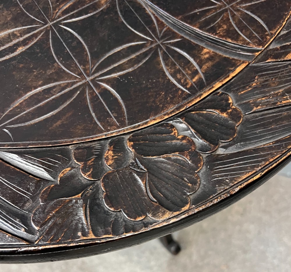 A circular dark ebonised wooden occasional table featuring a carved geometric top border with iris motifs, curved legs, and a small carved undertier shelf. View II