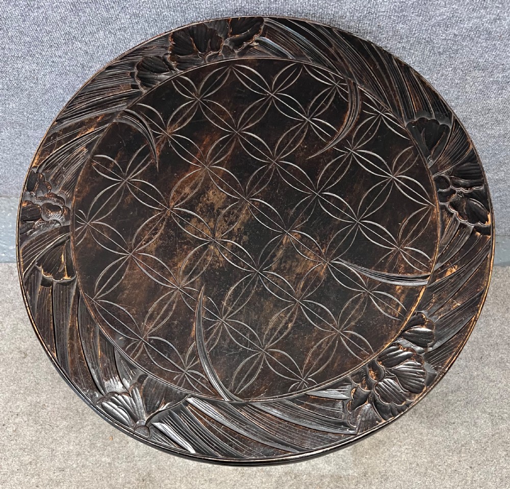 A circular dark ebonised wooden occasional table featuring a carved geometric top border with iris motifs, curved legs, and a small carved undertier shelf. View IV