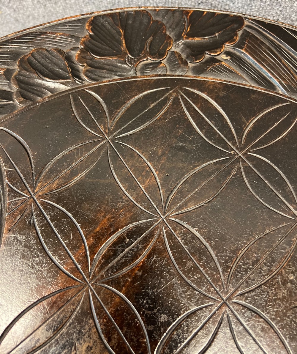 A circular dark ebonised wooden occasional table featuring a carved geometric top border with iris motifs, curved legs, and a small carved undertier shelf. View VII