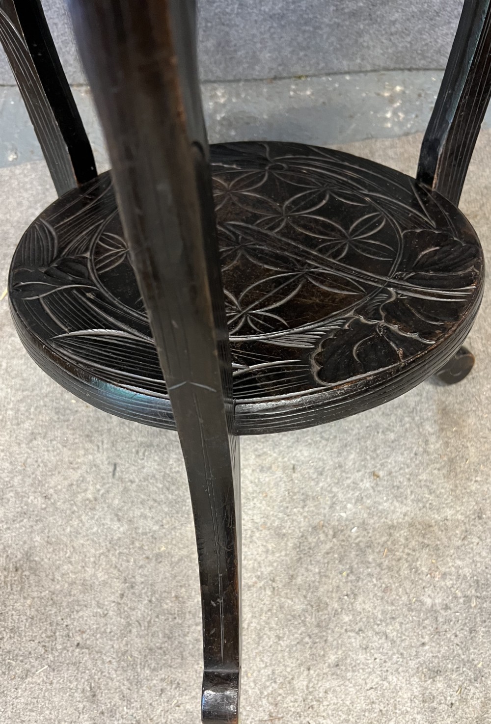 A circular dark ebonised wooden occasional table featuring a carved geometric top border with iris motifs, curved legs, and a small carved undertier shelf. View IX