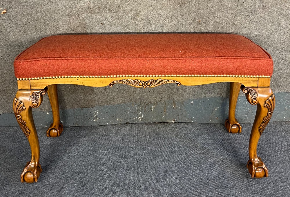 An upholstered window seat featuring a terracotta red fabric cushion with brass stud detailing, supported by carved walnut cabriole legs ending in claw and ball feet.