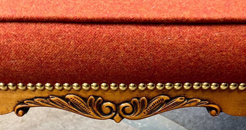 An upholstered window seat featuring a terracotta red fabric cushion with brass stud detailing, supported by carved walnut cabriole legs ending in claw and ball feet. View V