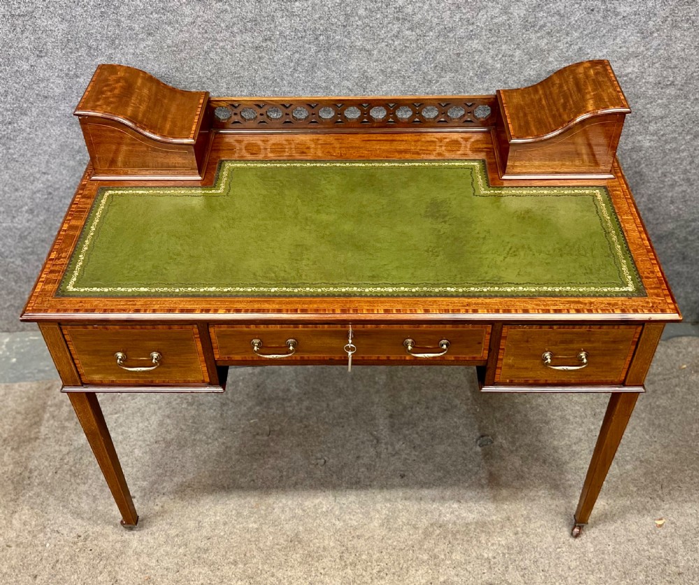 An Edwardian mahogany ladies writing desk featuring a green leather inset writing surface, inlaid crossbanding, three drawers with brass handles, twin raised stationery boxes, and tapered legs on castors. View II