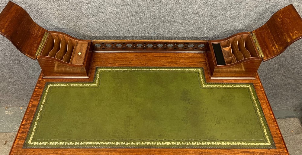 An Edwardian mahogany ladies writing desk featuring a green leather inset writing surface, inlaid crossbanding, three drawers with brass handles, twin raised stationery boxes, and tapered legs on castors. View V