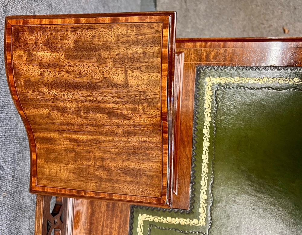 An Edwardian mahogany ladies writing desk featuring a green leather inset writing surface, inlaid crossbanding, three drawers with brass handles, twin raised stationery boxes, and tapered legs on castors. View VI