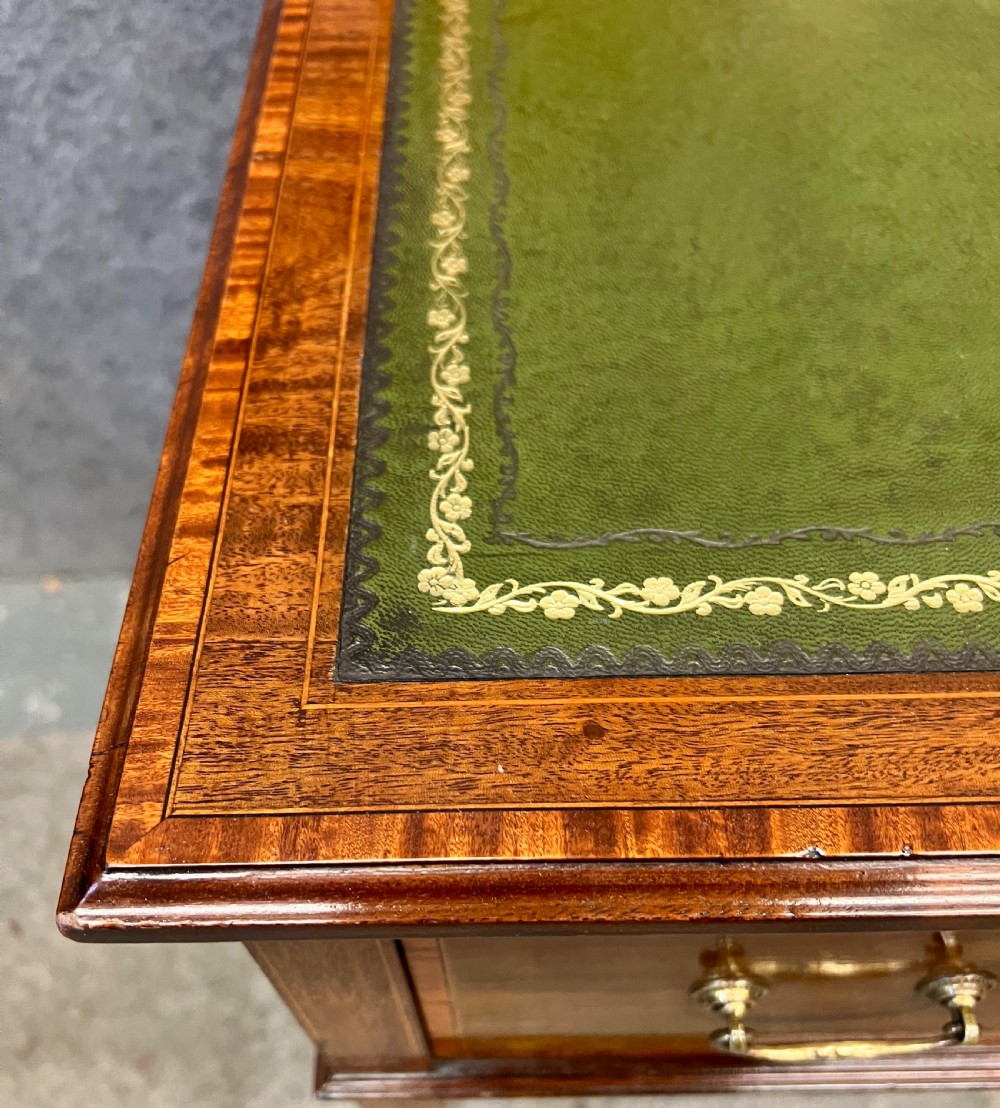 An Edwardian mahogany ladies writing desk featuring a green leather inset writing surface, inlaid crossbanding, three drawers with brass handles, twin raised stationery boxes, and tapered legs on castors. View IX