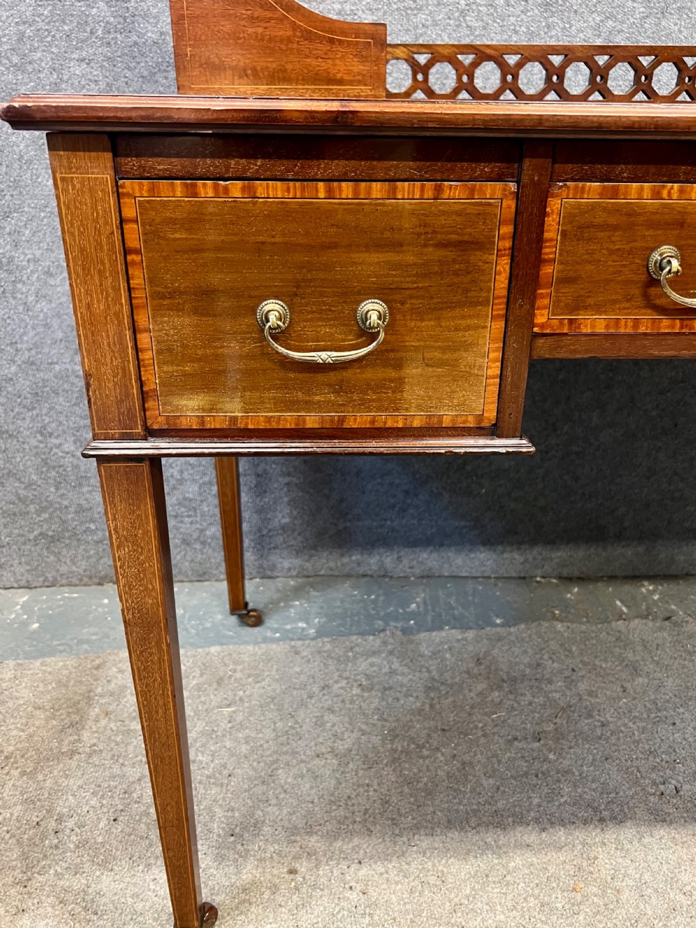 An Edwardian mahogany ladies writing desk featuring a green leather inset writing surface, inlaid crossbanding, three drawers with brass handles, twin raised stationery boxes, and tapered legs on castors. View X