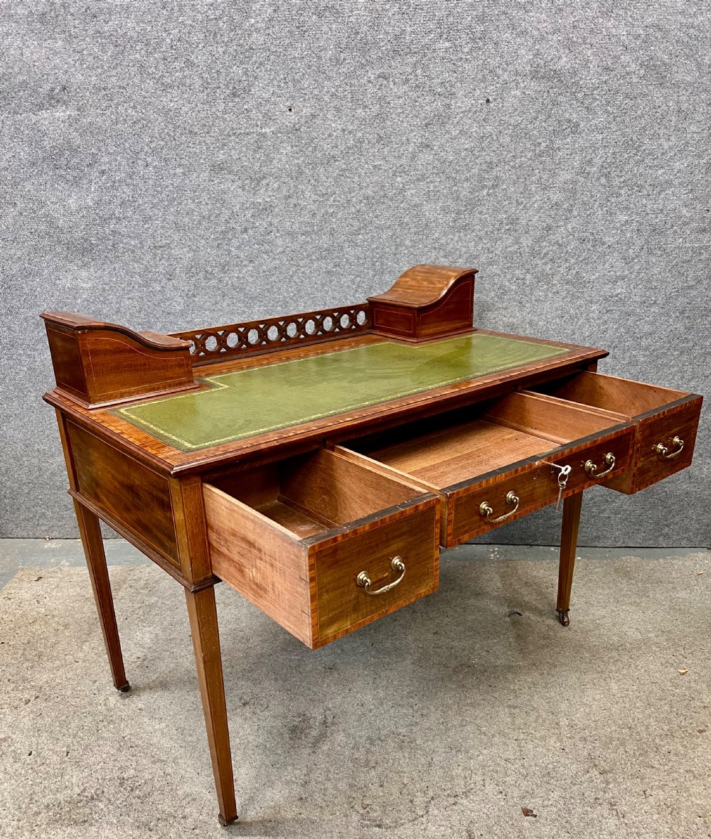 An Edwardian mahogany ladies writing desk featuring a green leather inset writing surface, inlaid crossbanding, three drawers with brass handles, twin raised stationery boxes, and tapered legs on castors. View XI