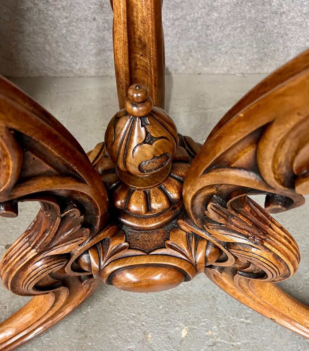 A circular Victorian centre table featuring a figured burr walnut top with carved egg-and-dart edge moulding, supported by a carved central pedestal with four splayed legs on ceramic castors. View III