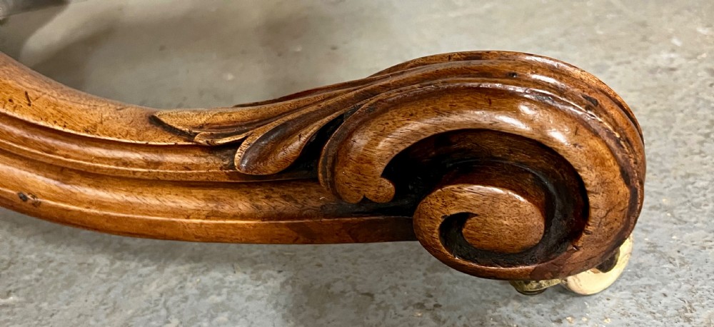 A circular Victorian centre table featuring a figured burr walnut top with carved egg-and-dart edge moulding, supported by a carved central pedestal with four splayed legs on ceramic castors. View V