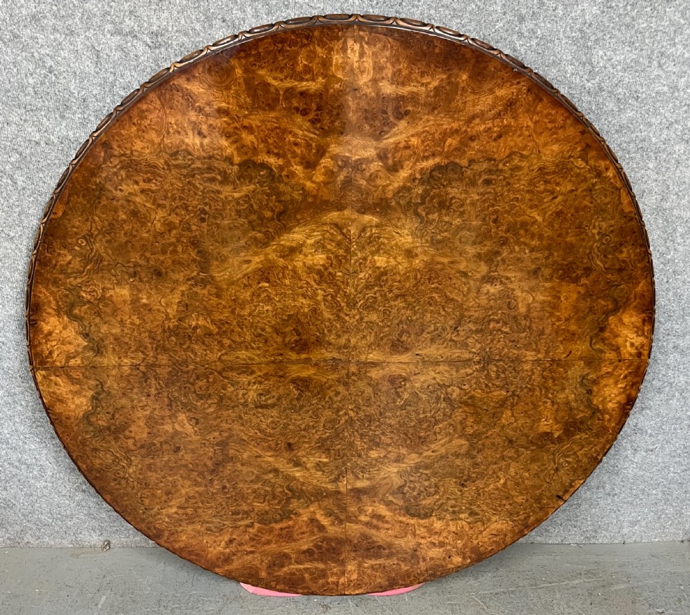 A circular Victorian centre table featuring a figured burr walnut top with carved egg-and-dart edge moulding, supported by a carved central pedestal with four splayed legs on ceramic castors. View VII
