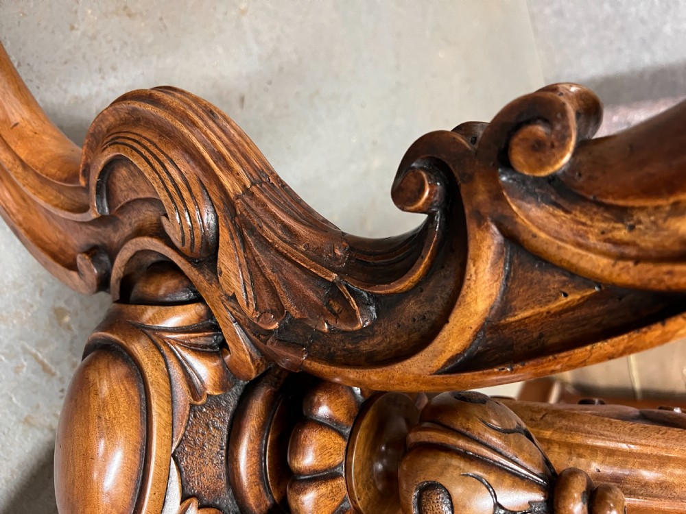 A circular Victorian centre table featuring a figured burr walnut top with carved egg-and-dart edge moulding, supported by a carved central pedestal with four splayed legs on ceramic castors. View X