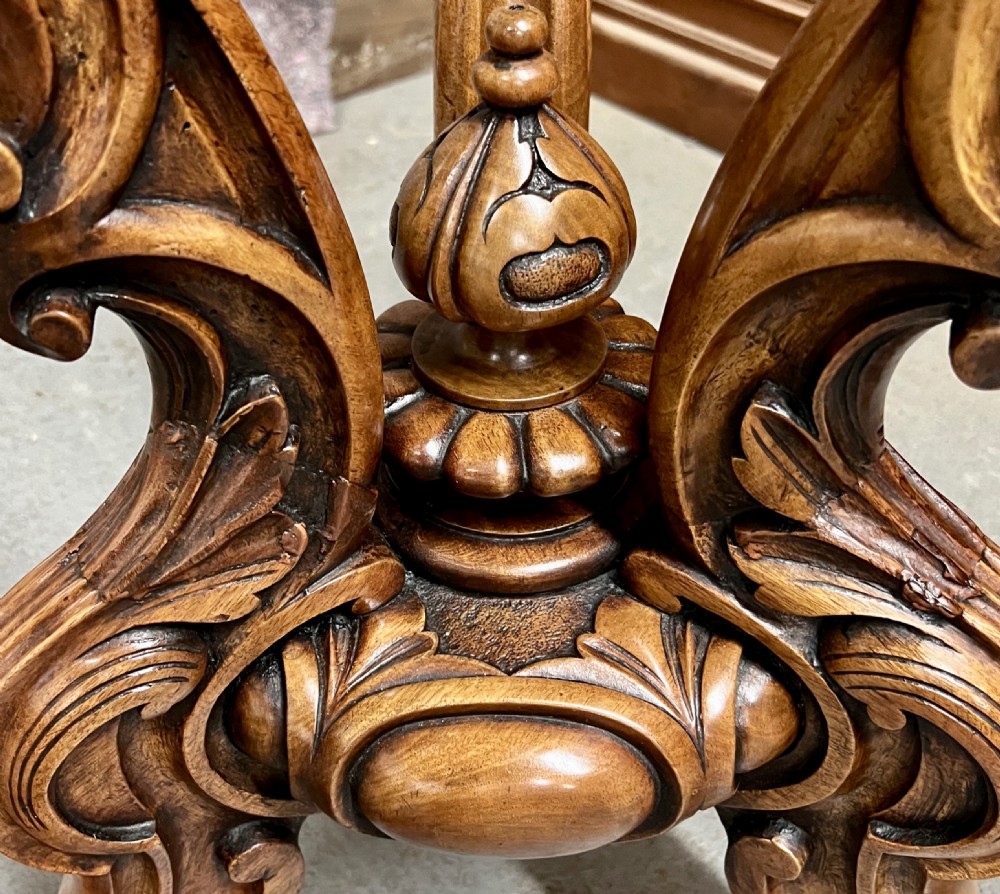 A circular Victorian centre table featuring a figured burr walnut top with carved egg-and-dart edge moulding, supported by a carved central pedestal with four splayed legs on ceramic castors. View XI