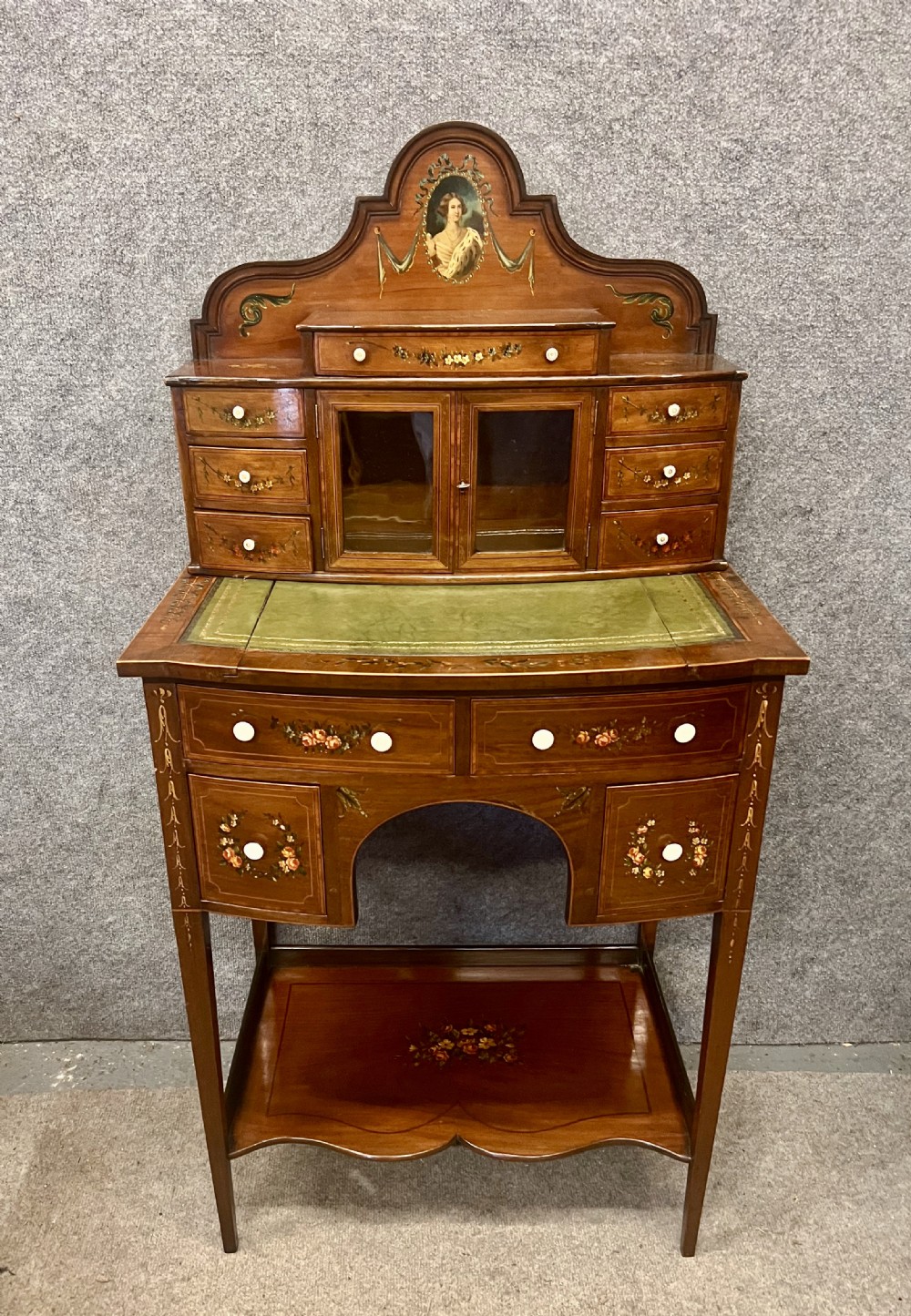 An Edwardian bonheur du jour desk crafted from polished dark wood, featuring a green leather writing surface, painted floral details, a upper superstructure with a painted portrait panel, small drawers, and a central glazed cabinet. View II