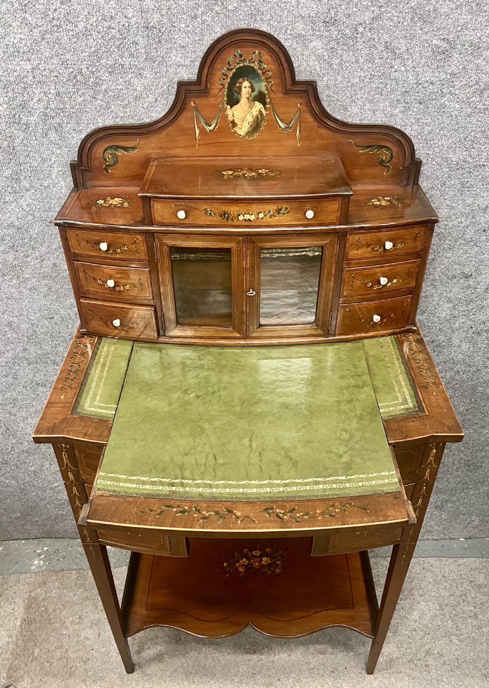 An Edwardian bonheur du jour desk crafted from polished dark wood, featuring a green leather writing surface, painted floral details, a upper superstructure with a painted portrait panel, small drawers, and a central glazed cabinet. View III