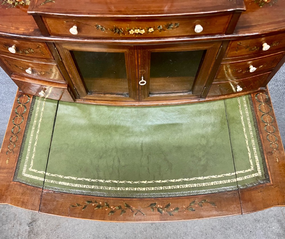 An Edwardian bonheur du jour desk crafted from polished dark wood, featuring a green leather writing surface, painted floral details, a upper superstructure with a painted portrait panel, small drawers, and a central glazed cabinet. View XI