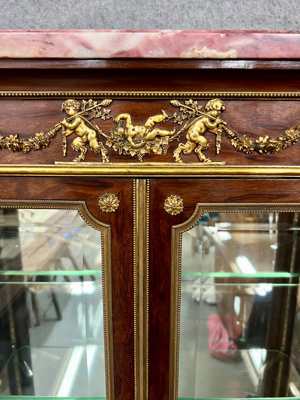 An antique French kingwood vitrine display cabinet featuring glazed double doors, gilt bronze ormolu mounts, glass shelves, a mirrored interior back, and a marble top. View III