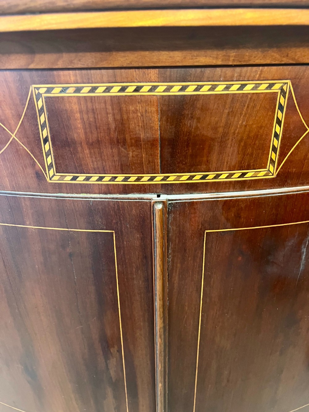 A George III mahogany bow-fronted hanging corner cabinet featuring double doors with fine stringing inlay and shield keyhole escutcheons. View II
