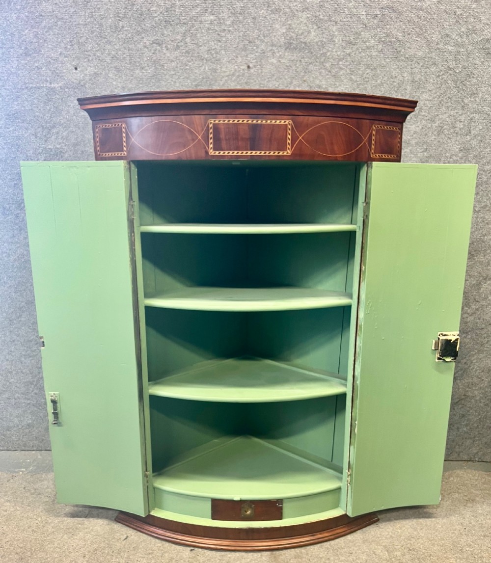 A George III mahogany bow-fronted hanging corner cabinet featuring double doors with fine stringing inlay and shield keyhole escutcheons. View IV