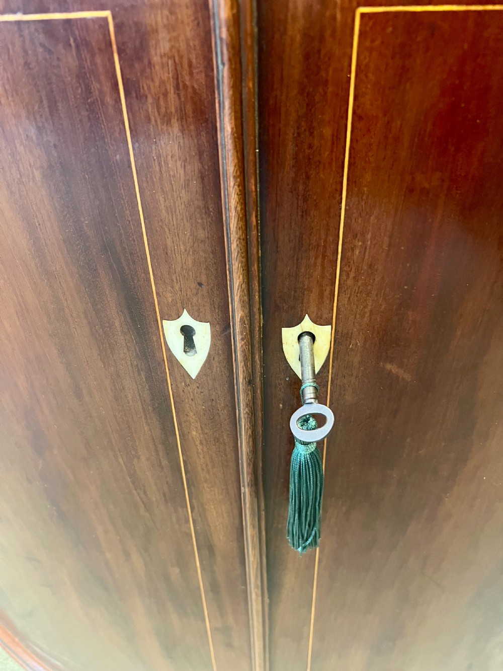 A George III mahogany bow-fronted hanging corner cabinet featuring double doors with fine stringing inlay and shield keyhole escutcheons. View VIII