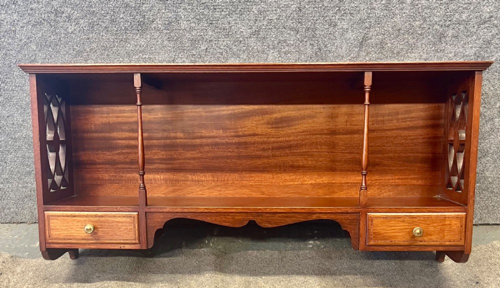An Edwardian mahogany hanging wall shelf featuring turned spindle supports, fretwork side panels, and two small inlaid drawers with brass knobs.