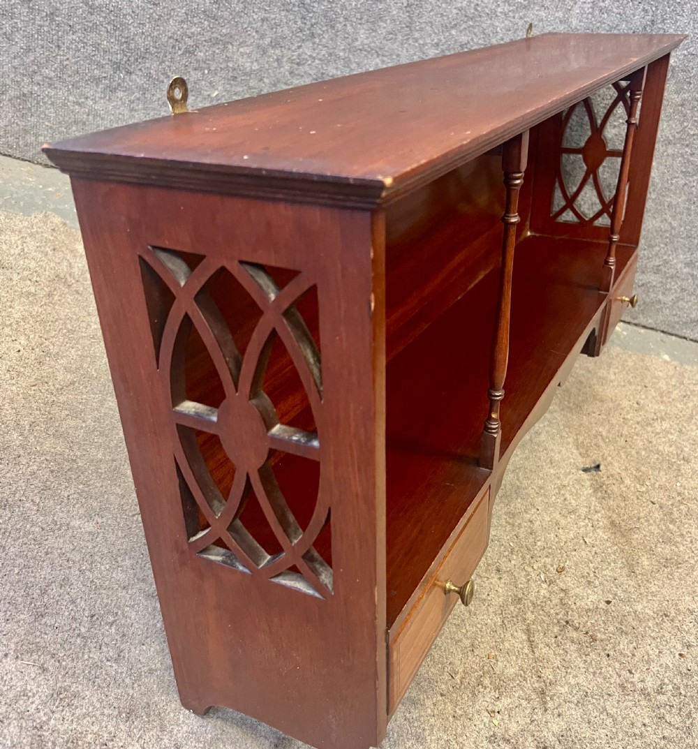 An Edwardian mahogany hanging wall shelf featuring turned spindle supports, fretwork side panels, and two small inlaid drawers with brass knobs. View III