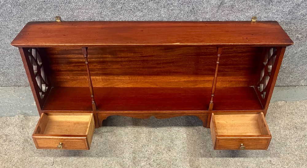 An Edwardian mahogany hanging wall shelf featuring turned spindle supports, fretwork side panels, and two small inlaid drawers with brass knobs. View IV