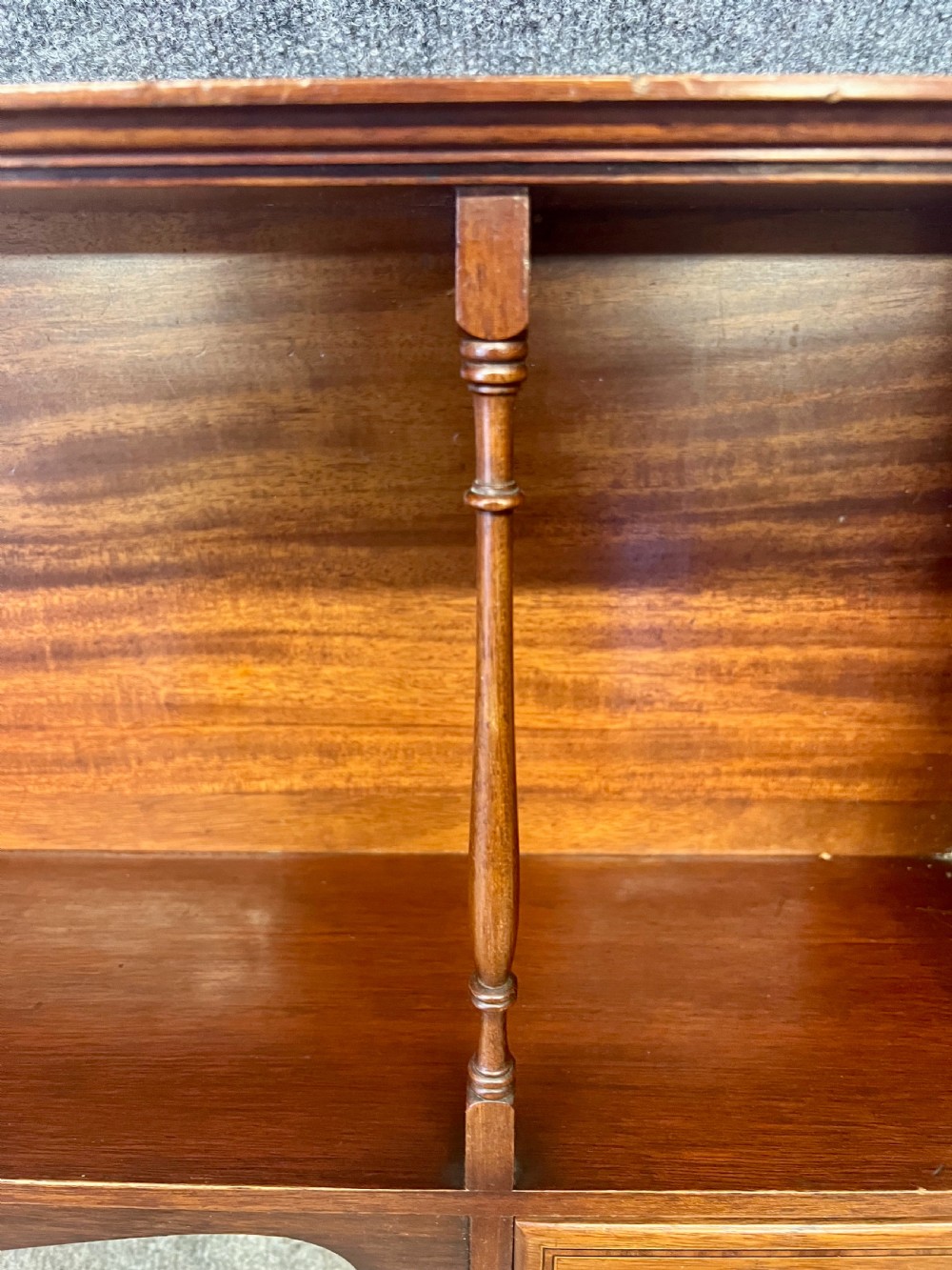 An Edwardian mahogany hanging wall shelf featuring turned spindle supports, fretwork side panels, and two small inlaid drawers with brass knobs. View VIII
