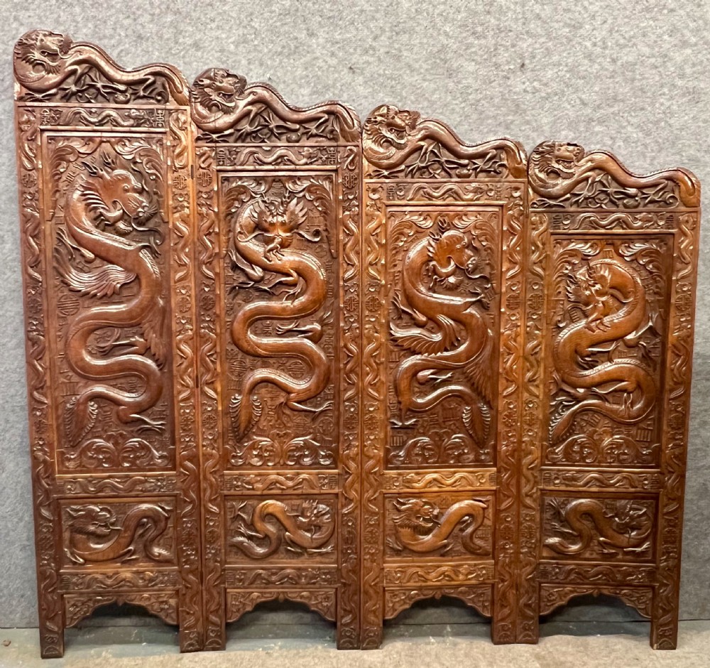 A four-panel carved hardwood folding room divider screen featuring relief dragon motifs and stepped top edges.