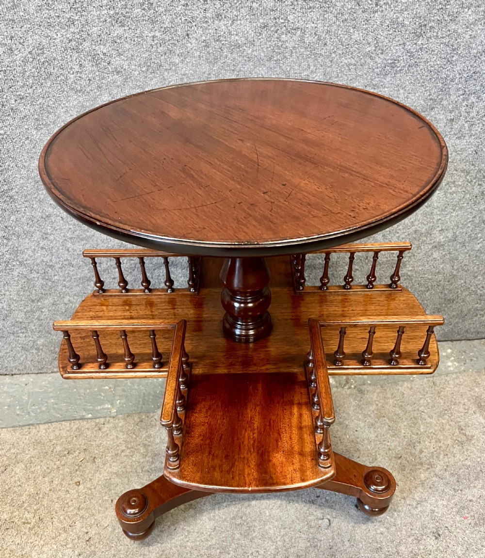 A circular mahogany revolving book mill table featuring a central turned column, four spindled book compartments, and a quadruped base.
