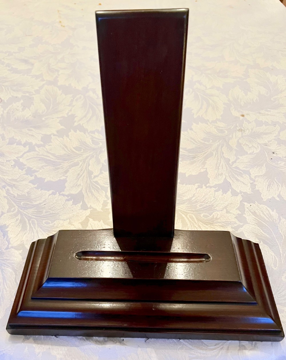 A dark polished mahogany weighted plate stand featuring a stepped moulded base with a central groove and a vertical upright backboard.