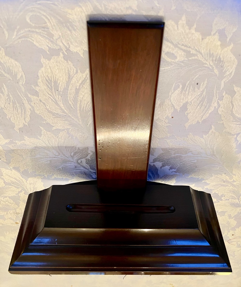 A dark polished mahogany weighted plate stand featuring a stepped moulded base with a central groove and a vertical upright backboard. View II