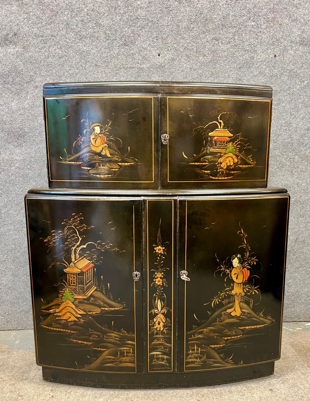 A two-tier black lacquered Art Deco cocktail cabinet featuring hand-painted gold and polychrome Chinoiserie figures and landscapes.