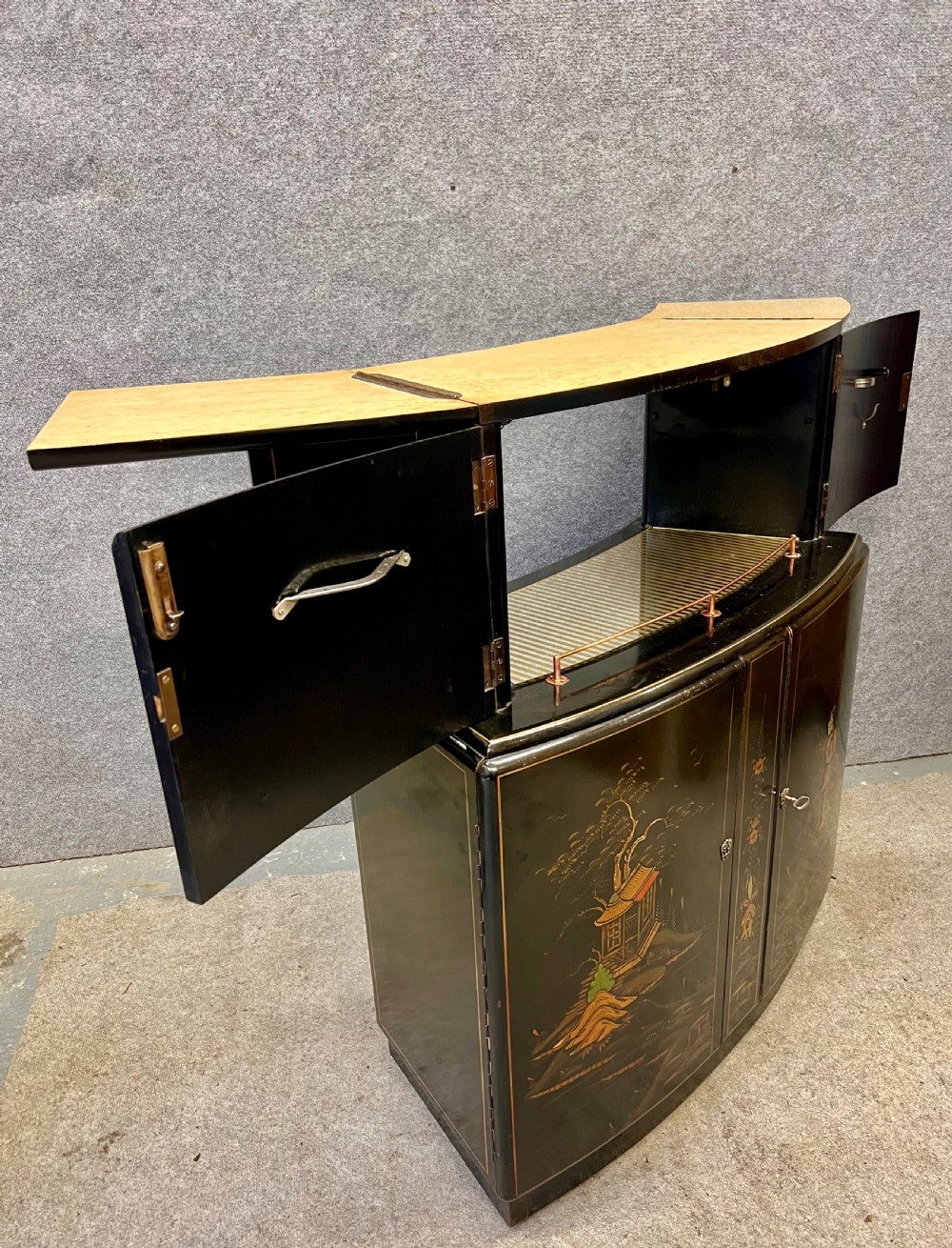 A two-tier black lacquered Art Deco cocktail cabinet featuring hand-painted gold and polychrome Chinoiserie figures and landscapes. View X