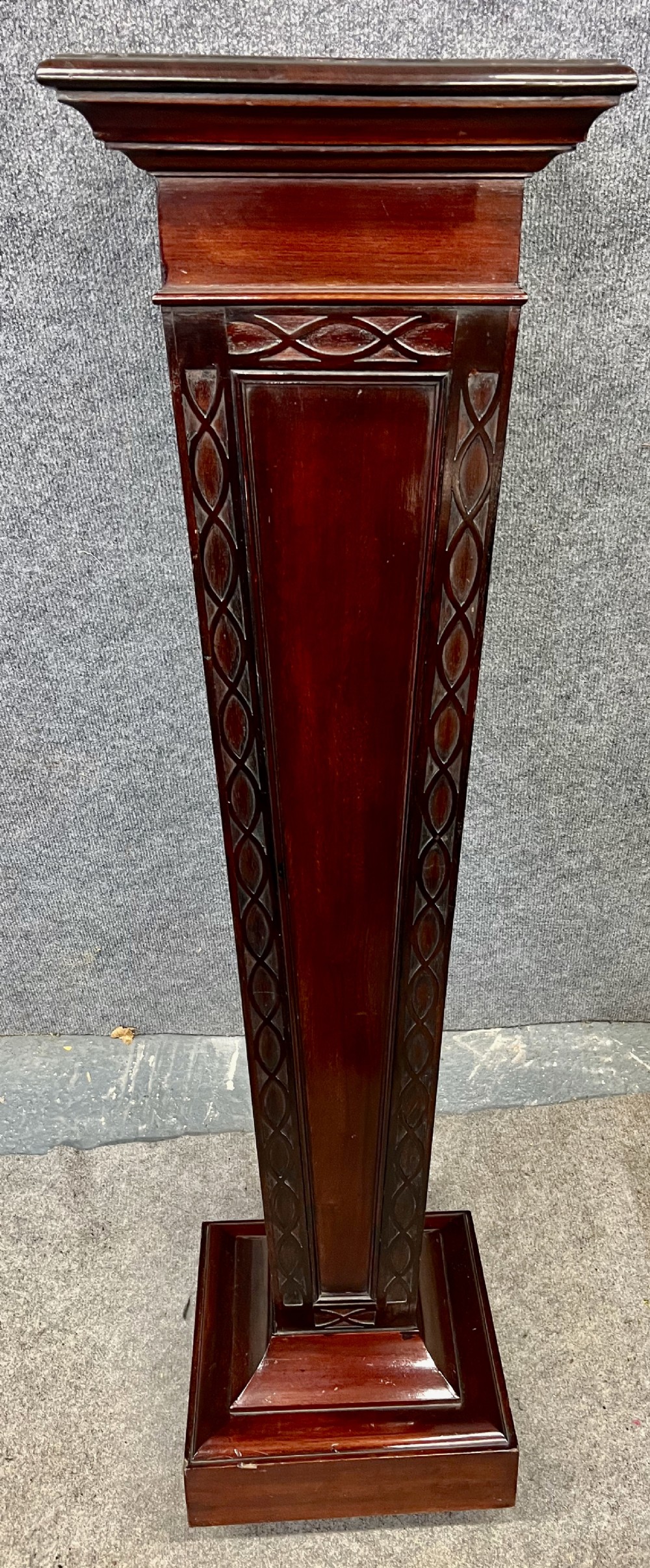 A tall, tapered mahogany pedestal featuring a square moulded top, carved strapwork border details, and a stepped plinth base.