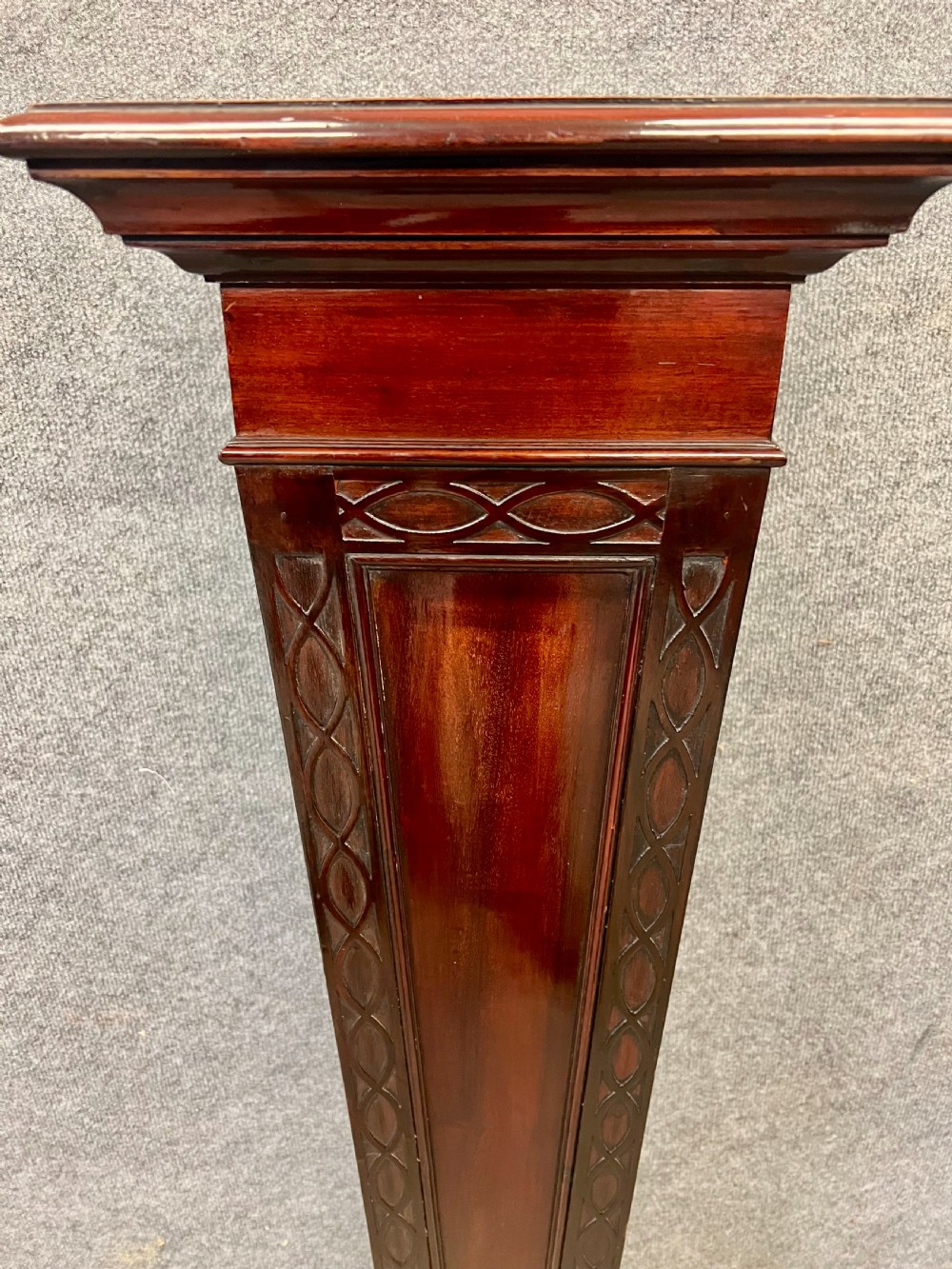 A tall, tapered mahogany pedestal featuring a square moulded top, carved strapwork border details, and a stepped plinth base. View IV