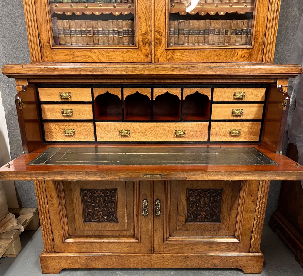 A two-tier Victorian pollard oak secretaire bookcase featuring upper glazed doors with books above a lower cabinet with carved relief panels. View V