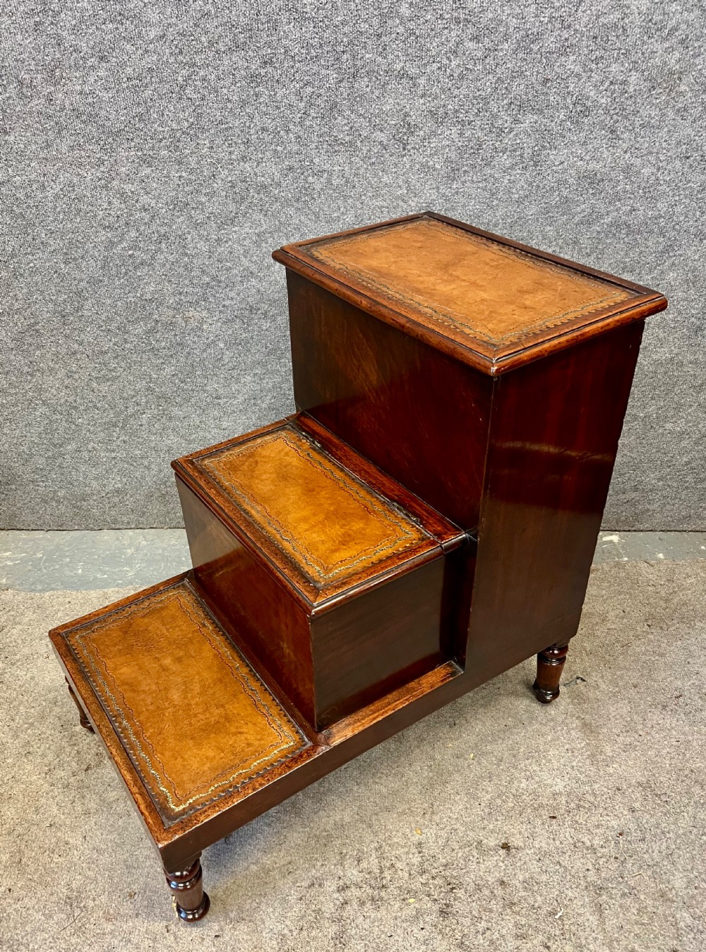 A set of three dark mahogany library steps featuring gold-tooled tan leather treads and turned wooden legs.