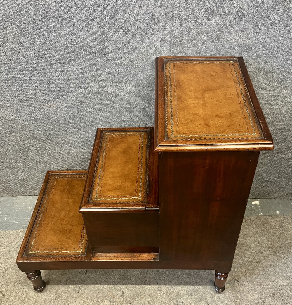 A set of three dark mahogany library steps featuring gold-tooled tan leather treads and turned wooden legs. View V