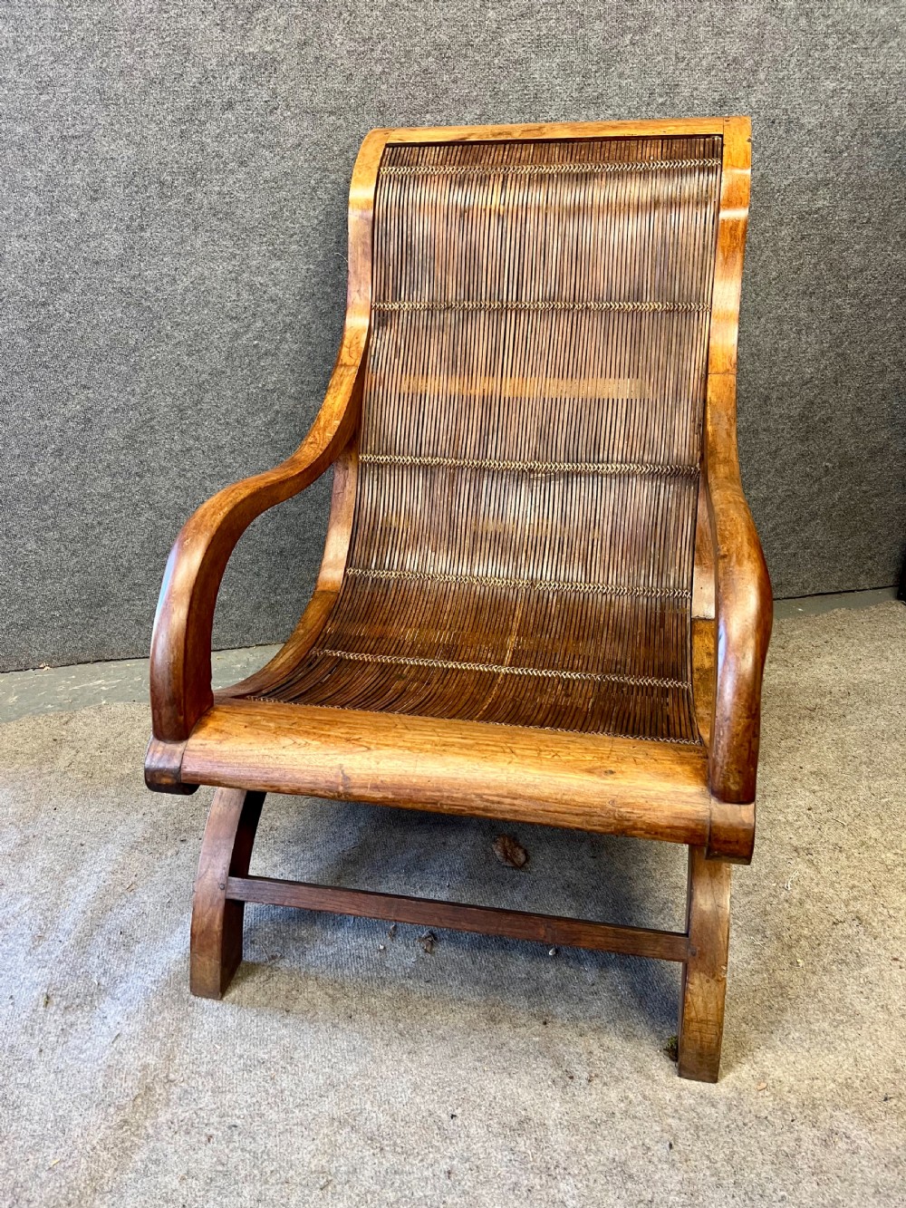 A pair of teak plantation chairs with reclining frames, woven split cane backs and seats, turned front legs, and flat extended armrests. View II