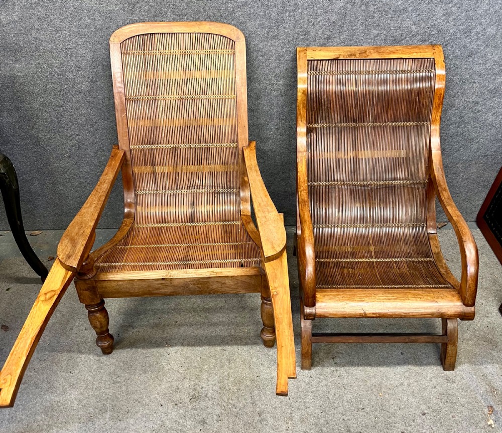 A pair of teak plantation chairs with reclining frames, woven split cane backs and seats, turned front legs, and flat extended armrests.