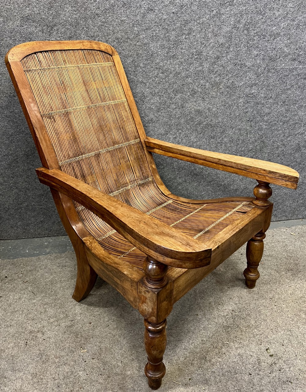 A pair of teak plantation chairs with reclining frames, woven split cane backs and seats, turned front legs, and flat extended armrests. View IV