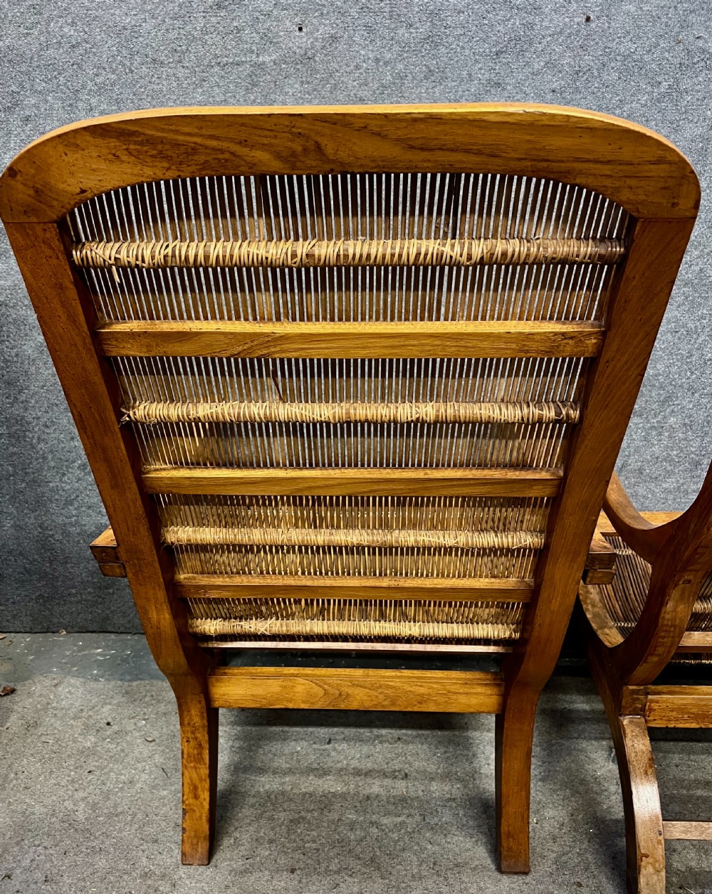 A pair of teak plantation chairs with reclining frames, woven split cane backs and seats, turned front legs, and flat extended armrests. View VII