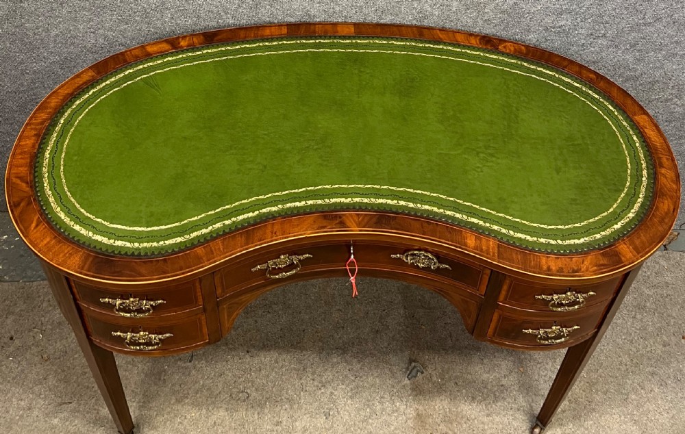 An Edwardian mahogany kidney-shaped desk with a green leather insert top, satinwood inlay, five drawers, and tapered legs on brass castors. View IV