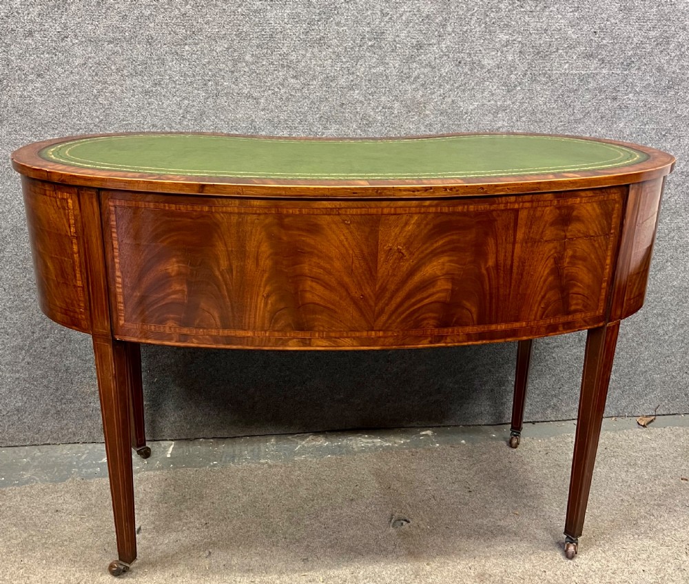 An Edwardian mahogany kidney-shaped desk with a green leather insert top, satinwood inlay, five drawers, and tapered legs on brass castors. View VII