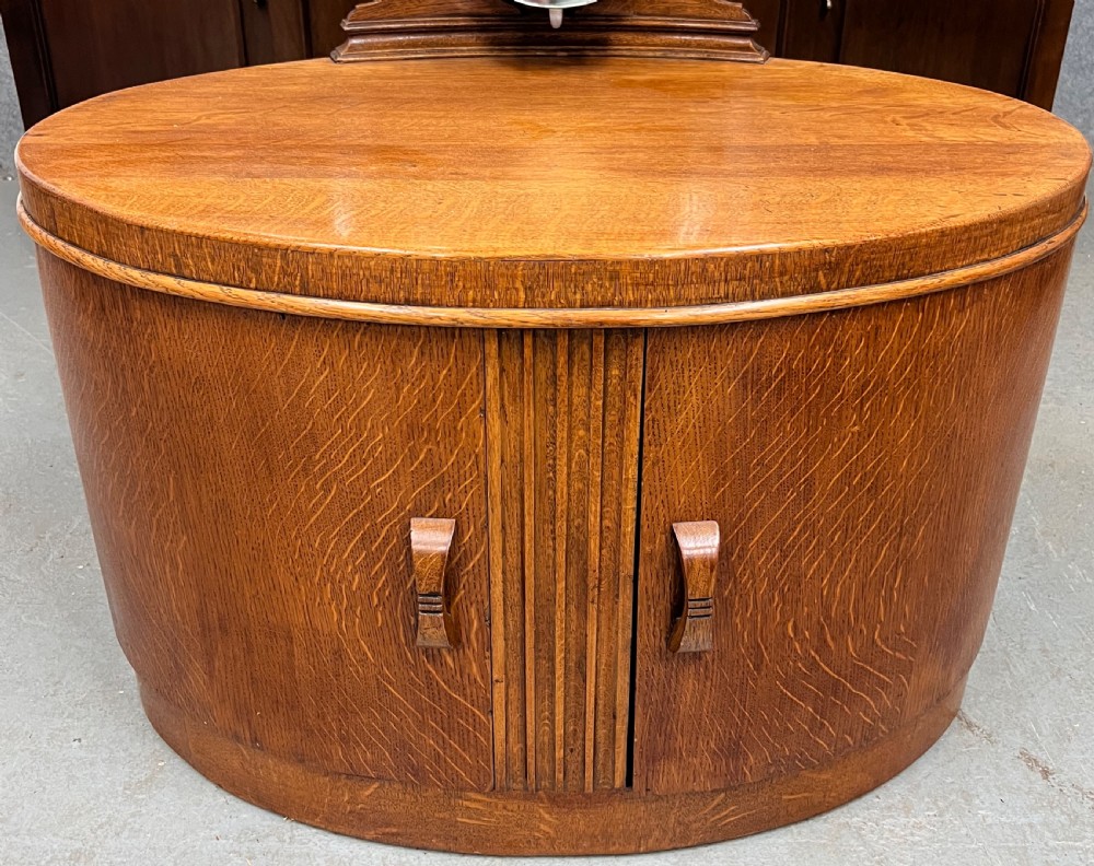 An Art Deco golden oak dressing table with an oval drum base, carved geometric handles, and an attached tall oval tripartite mirror. View II