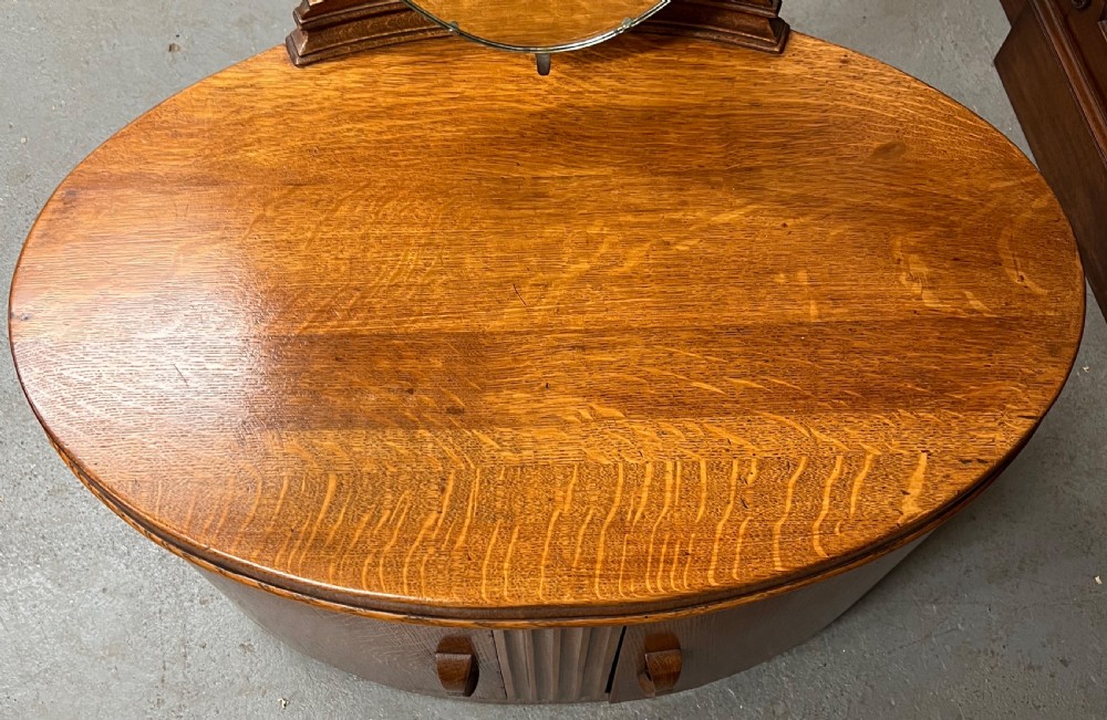 An Art Deco golden oak dressing table with an oval drum base, carved geometric handles, and an attached tall oval tripartite mirror. View V